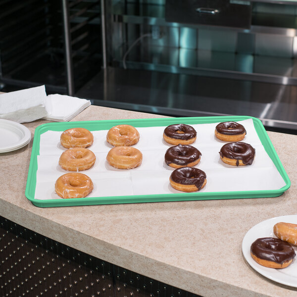 A Carlisle tropical green Glasteel bakery display tray of chocolate covered donuts on a counter.