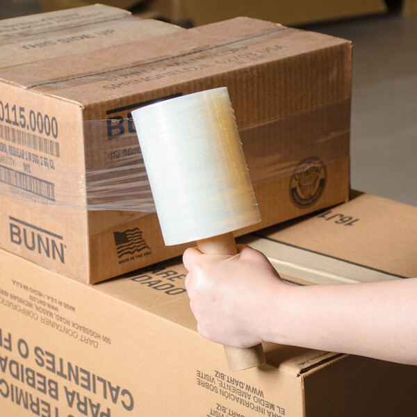 A hand holding a roll of 5" x 1000' disposable banding film on a stack of boxes.