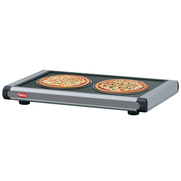 A Hatco heated shelf with pizza pans holding pizzas on a table in a pizza parlor.