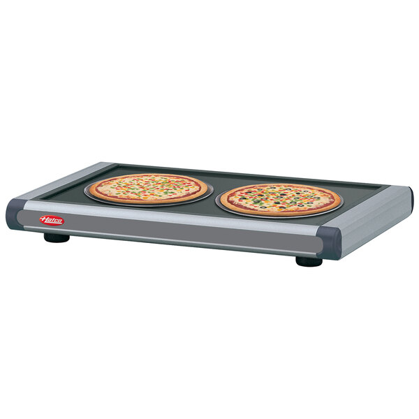 A Hatco heated shelf with dark gray caps holding two pizzas on a pan.