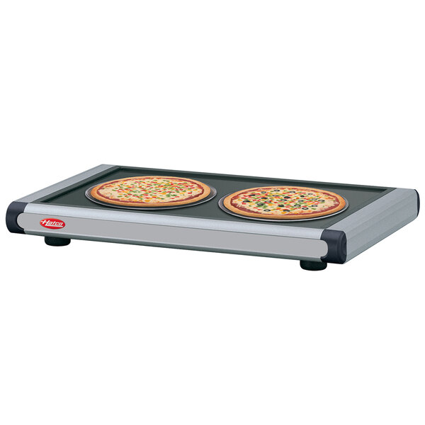 Two pizzas on a Hatco heated shelf with black caps.