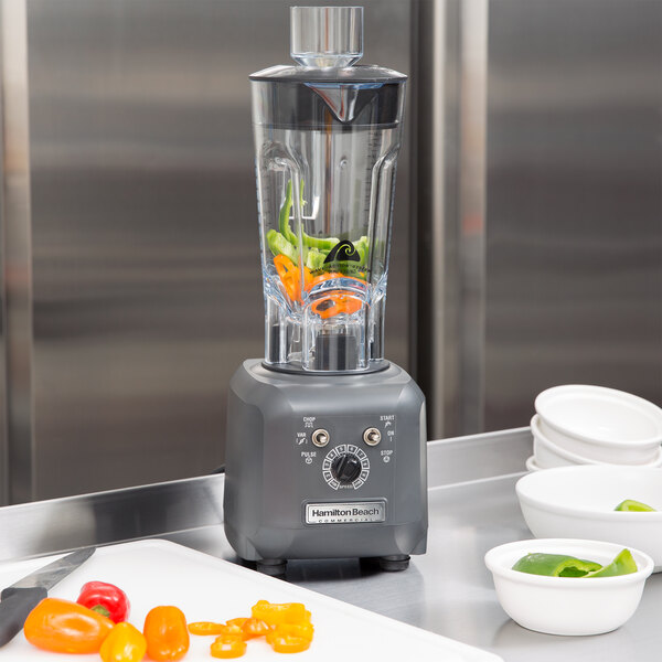 A Hamilton Beach food blender with green peppers in it.