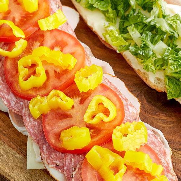 A sandwich with tomatoes and Regal mild banana pepper rings on top on a cutting board.