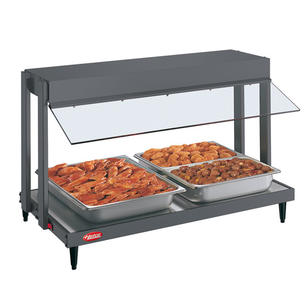 A Hatco mini-merchandising warmer with two trays of food on a table with a glass top.