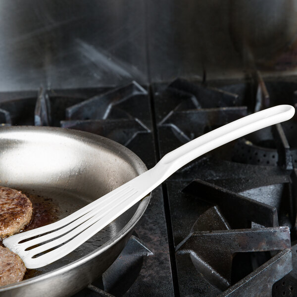 A white slotted turner on a frying pan with meat.