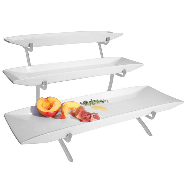 A Cal-Mil three tier wire riser with white porcelain plates holding fruit and vegetables.