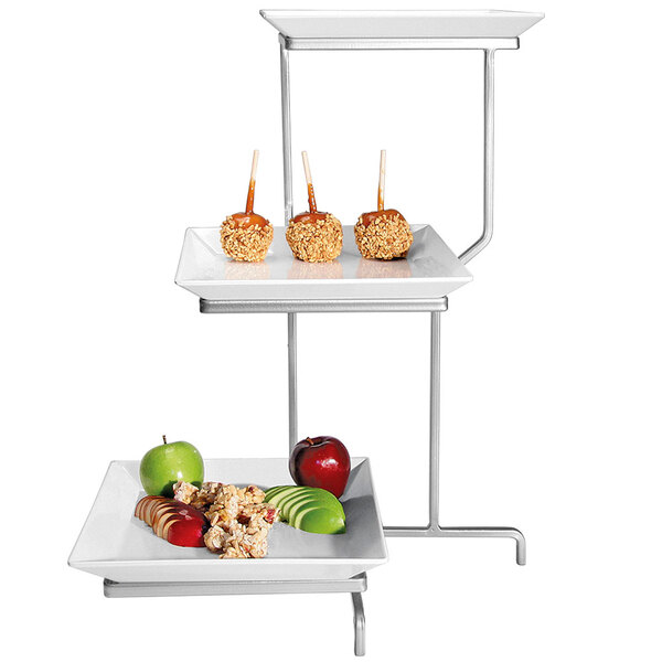 A Cal-Mil three tiered display with square plates holding green apples and a tray of fruit and candy.