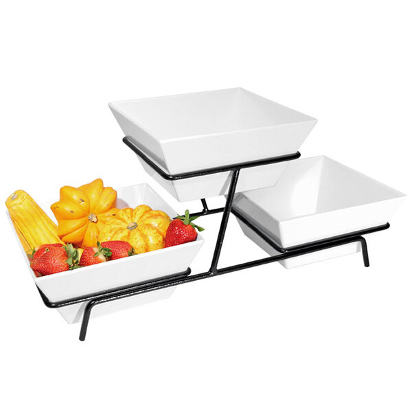 A black metal two tier wire stand with white square bowls filled with fruit.