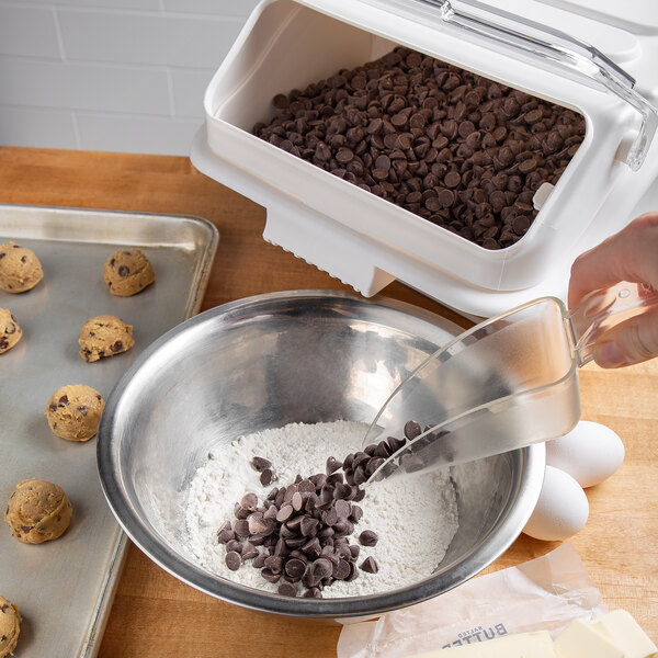 A person using a Cal-Mil polycarbonate scoop to measure chocolate chips into a bowl.