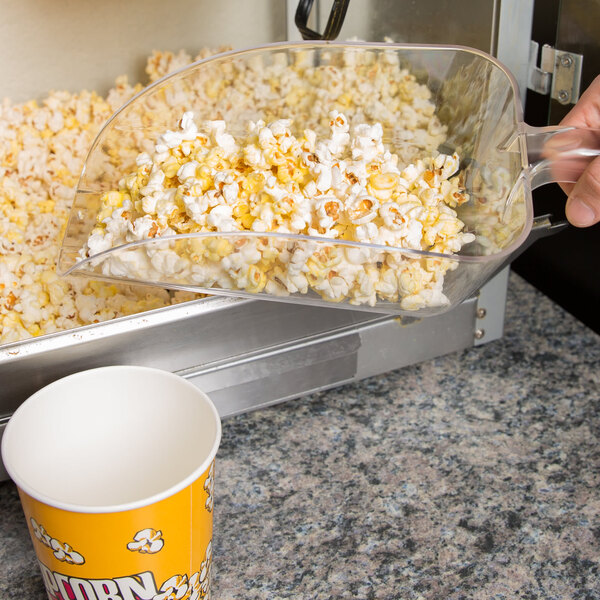 A hand using a Cal-Mil polycarbonate scoop to pour popcorn into a bowl.