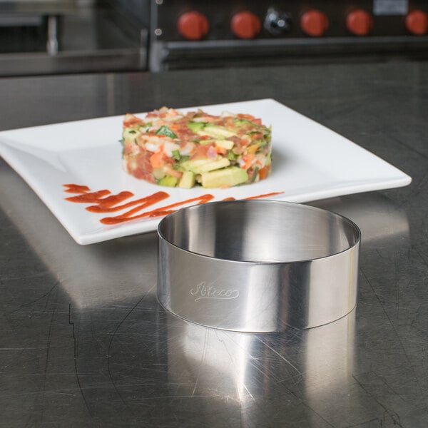 A stainless steel oval mold on a counter with food on a plate.