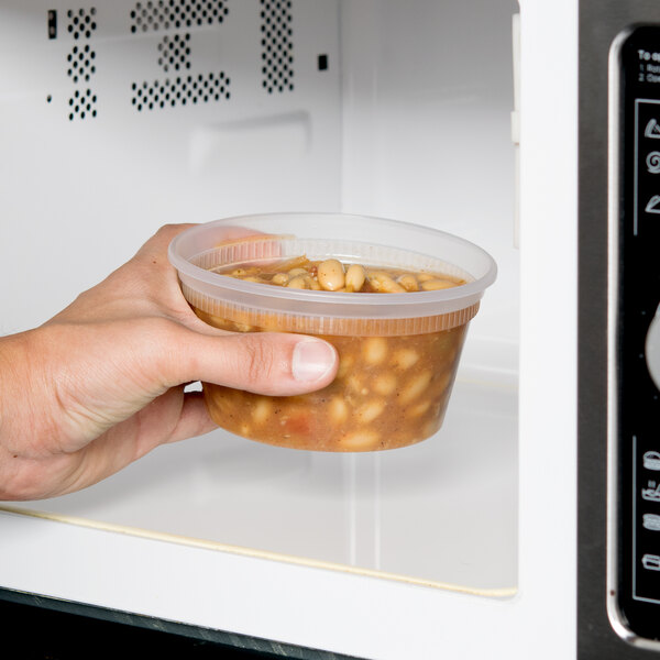 A hand holding a Pactiv Delitainer of beans in a microwave.