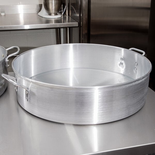 A Town aluminum water pan with a lid on a stainless steel surface filled with water.
