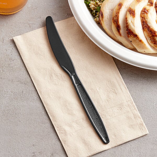 A Visions black plastic knife on a napkin next to a plate of food.