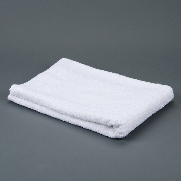 A folded white Oxford Bronze bath towel on a gray surface.