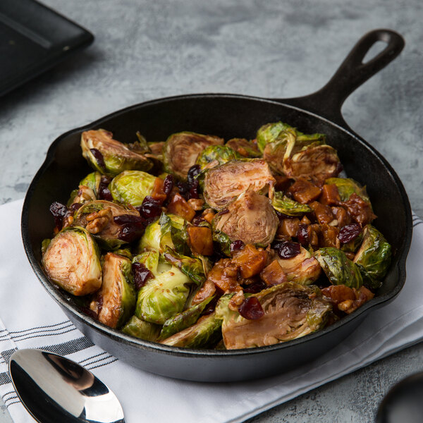 A Lodge pre-seasoned cast iron skillet filled with brussels sprouts, cranberries, and bacon on a table.