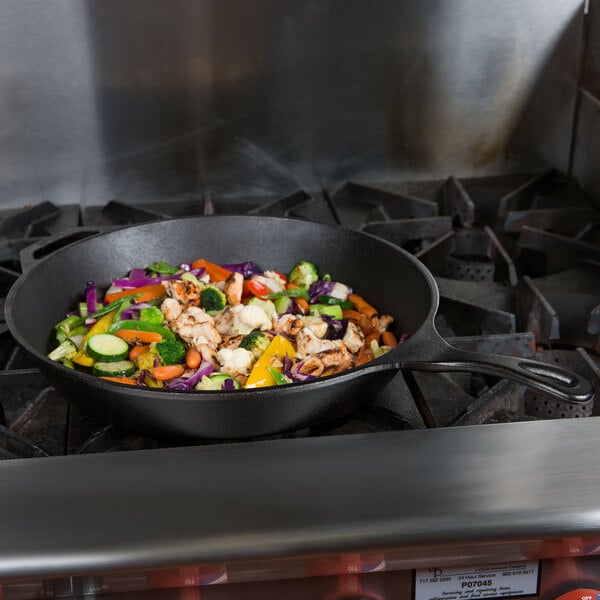 A Lodge cast iron skillet filled with vegetables cooking on a stove.
