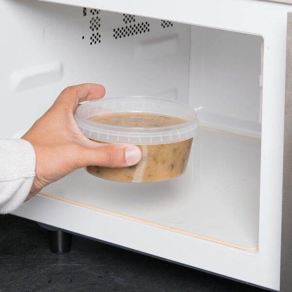 A hand holding a clear Tamper Resistant Deli Container of food