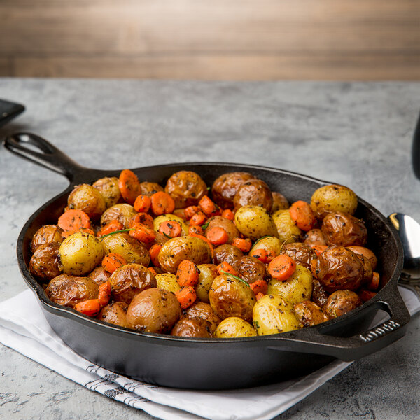 A Lodge cast iron skillet with potatoes and carrots cooking in it.