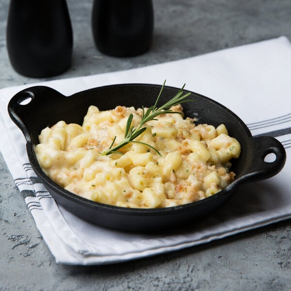 A Lodge mini cast iron round casserole dish filled with macaroni and cheese on a white table.