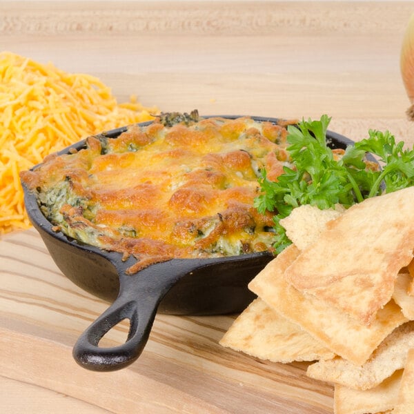 A Lodge mini cast iron skillet of food with cheese and crackers on a table.