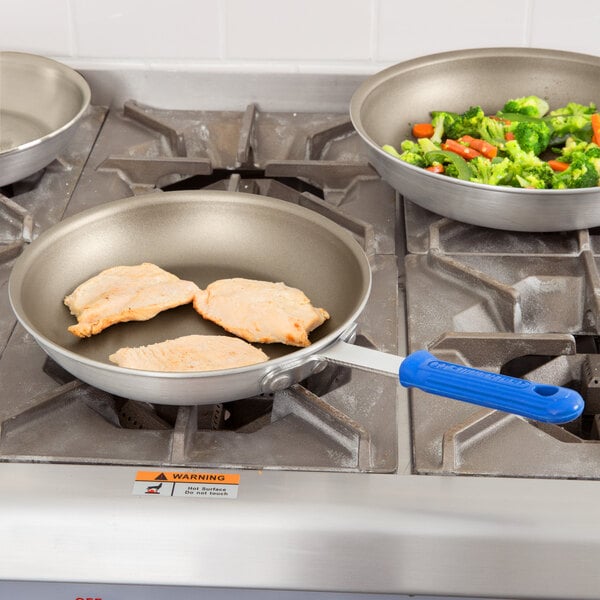 A Vollrath Wear-Ever aluminum non-stick fry pan with a blue Cool Handle cooking chicken and vegetables on a stove.