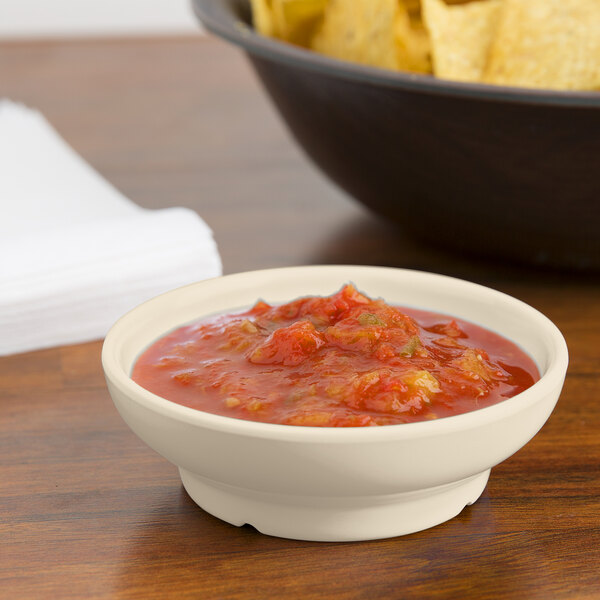 An ivory melamine salsa dish filled with salsa next to a bowl of chips.