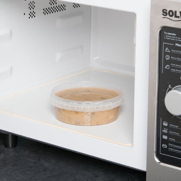 A clear plastic deli container of soup in a microwave.