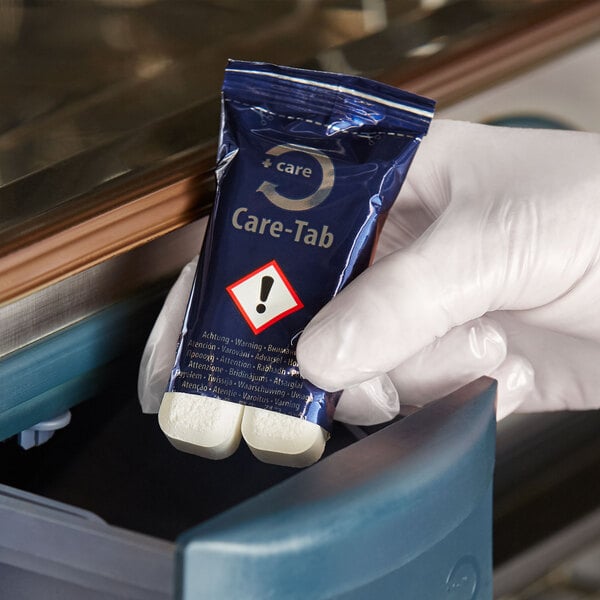 A hand in a white glove holding a blue package of Rational Care Tabs.