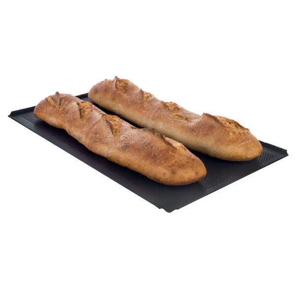 A pair of long loaves of bread on a black perforated baking tray.