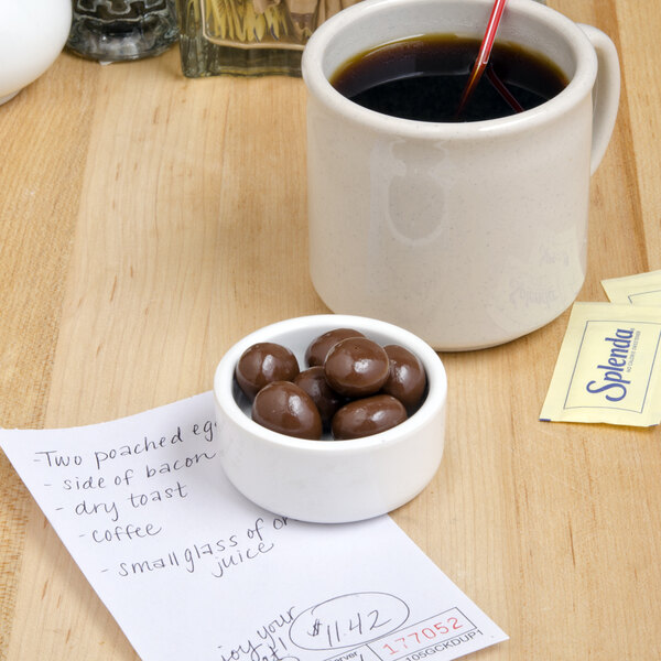 A bowl of DaVinci Gourmet milk chocolate covered espresso beans on a table with a cup of coffee.