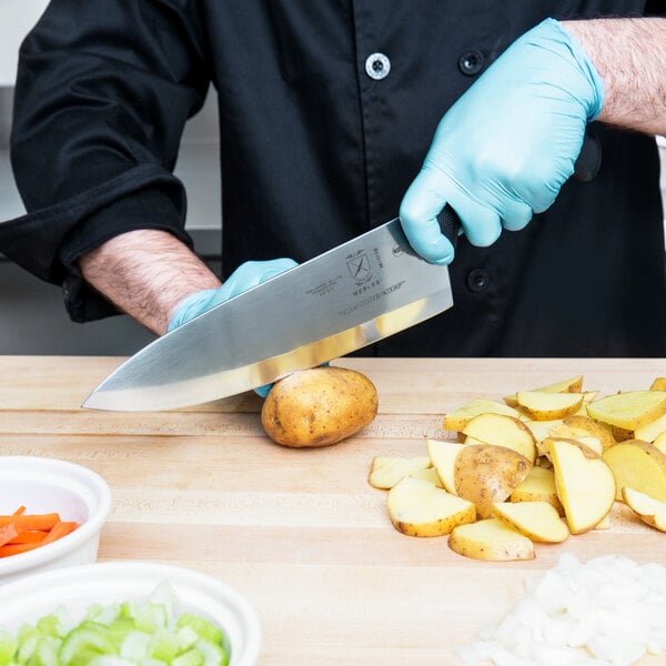 A person using a Mercer Culinary Millennia Chef Knife to cut potatoes on a cutting board.