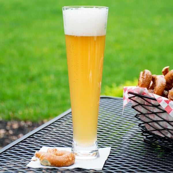 A Carlisle plastic pilsner glass filled with beer on a table outdoors.