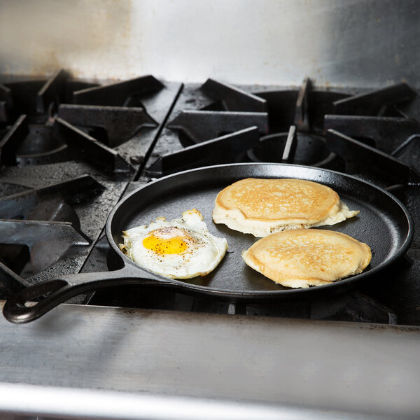A Lodge cast iron griddle with two pancakes and a fried egg cooking on a stovetop.