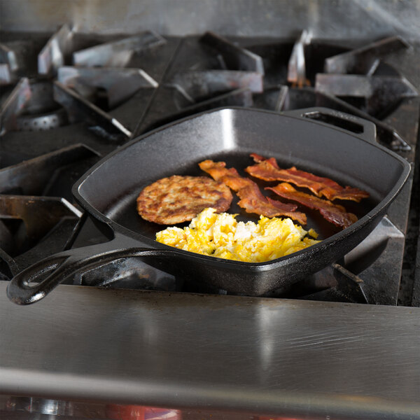 A Lodge square cast iron skillet with eggs and bacon cooking on top of a stove.