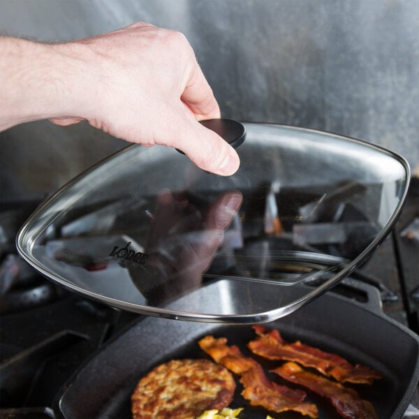 A person using a Lodge square tempered glass cover on a frying pan.