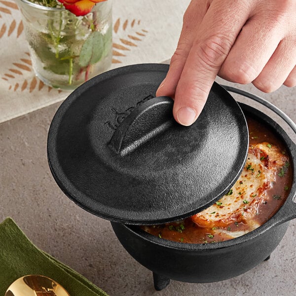 A person using a Lodge cast iron lid on a pot of food.