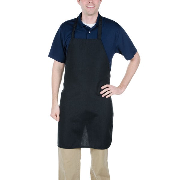 A man wearing a black Chef Revival bib apron in a professional kitchen.