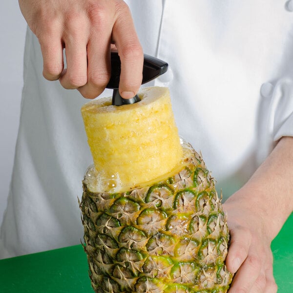 A hand using the Vacu Vin 3-in-1 Pineapple Corer/Slicer/Peeler to cut and peel a pineapple