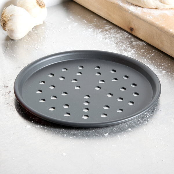 An American Metalcraft black round pizza pan with holes on it.