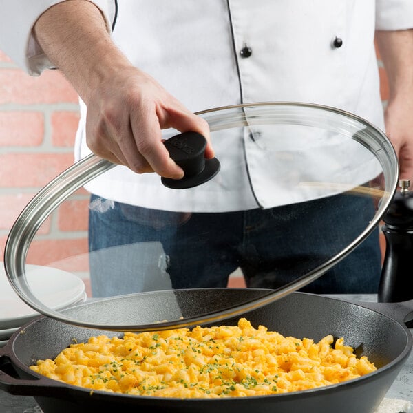 A person using a Lodge tempered glass cover to cook food in a cast iron skillet.