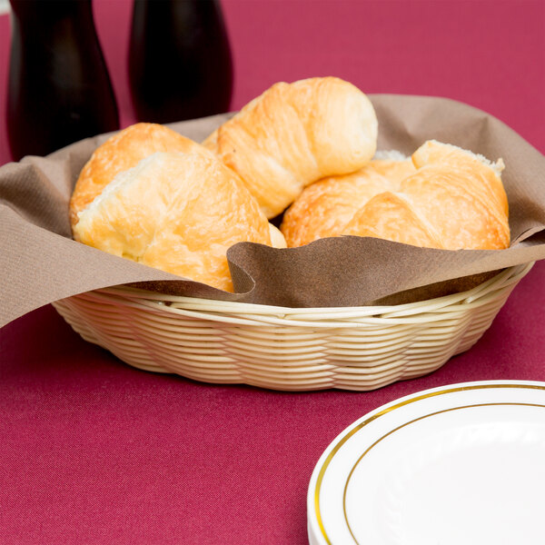 A Thunder Group rattan bread basket on a table with croissants.