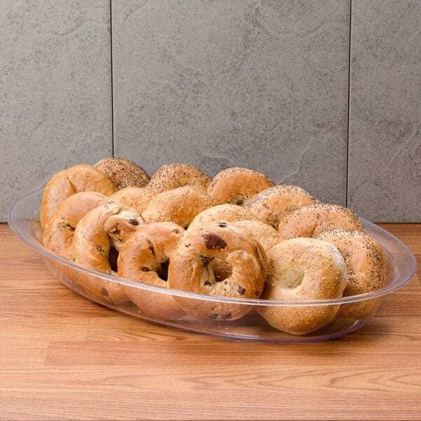 A clear plastic oval bowl filled with bagels on a table.