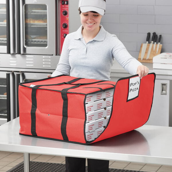 A woman holding a red pizza bag with white boxes inside.