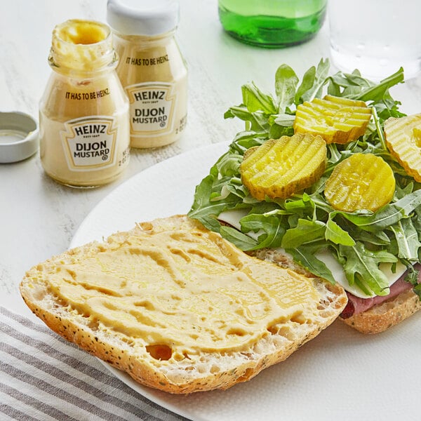 A sandwich with pickles and cheese on a plate with a bottle of Heinz Dijon Mustard.