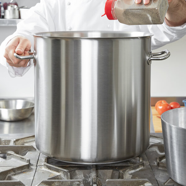A chef pouring seasoning into a large Vollrath stainless steel stock pot.