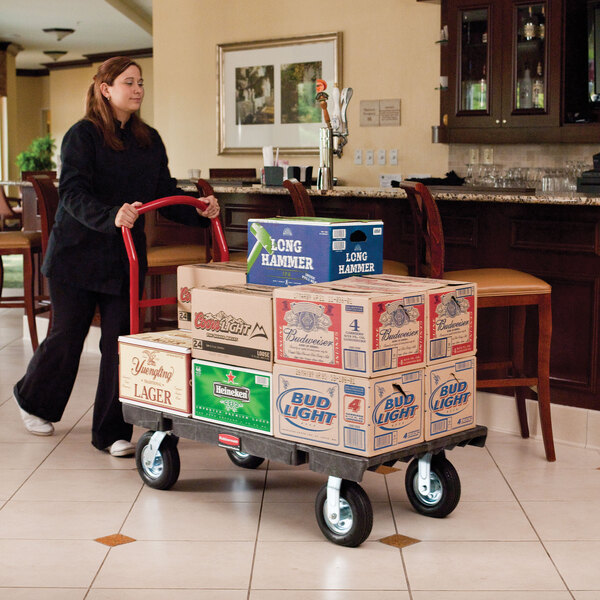 A woman pushing a Rubbermaid platform truck with boxes on it.