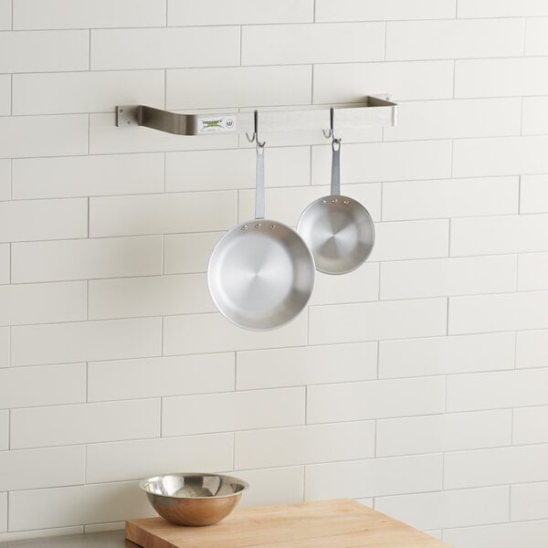 A stainless steel Regency pot rack holding pans on a wall.