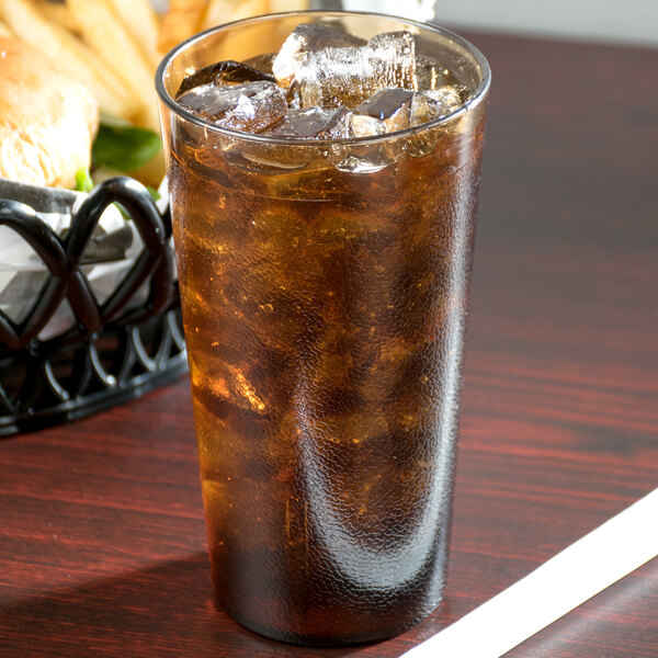 A Cambro amber plastic tumbler filled with ice tea on a table with a basket of food.