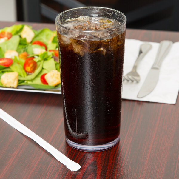 A Cambro clear plastic tumbler filled with ice and soda on a table with a salad.